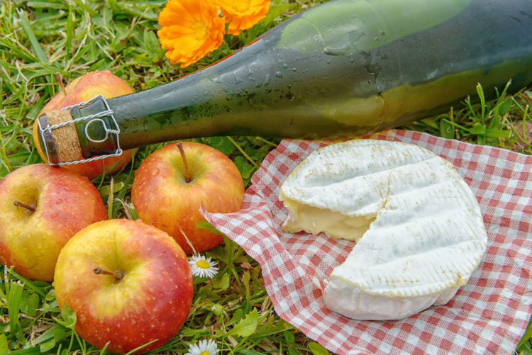 several apples with cider and camembert in the grass